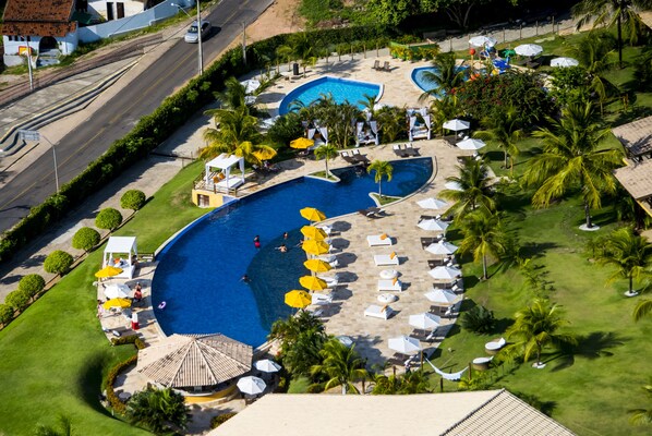 Vista aérea de un complejo turístico con una gran piscina, tumbonas y palmeras.