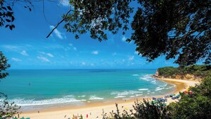 A beach with umbrellas and people, surrounded by greenery. - Pipa Lagoa Hotel (Tibau do Sul)