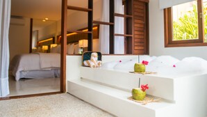 A modern hotel room with a large bed, a white sofa, and a small table with decorative items. - Pipa Lagoa Hotel (Tibau do Sul)