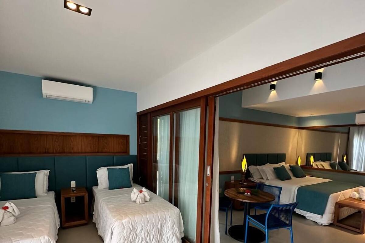 Ett hotellrum med två sängar, ett litet bord och en soffa. Det finns en skjutdörr i glas som leder till ett större rum med ett biljardbord.