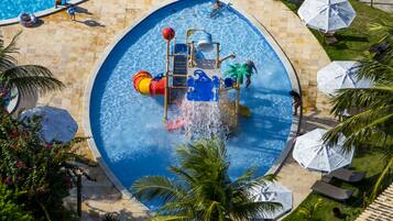 Una piscina con zona de juegos acuáticos, palmeras y sillas de descanso.