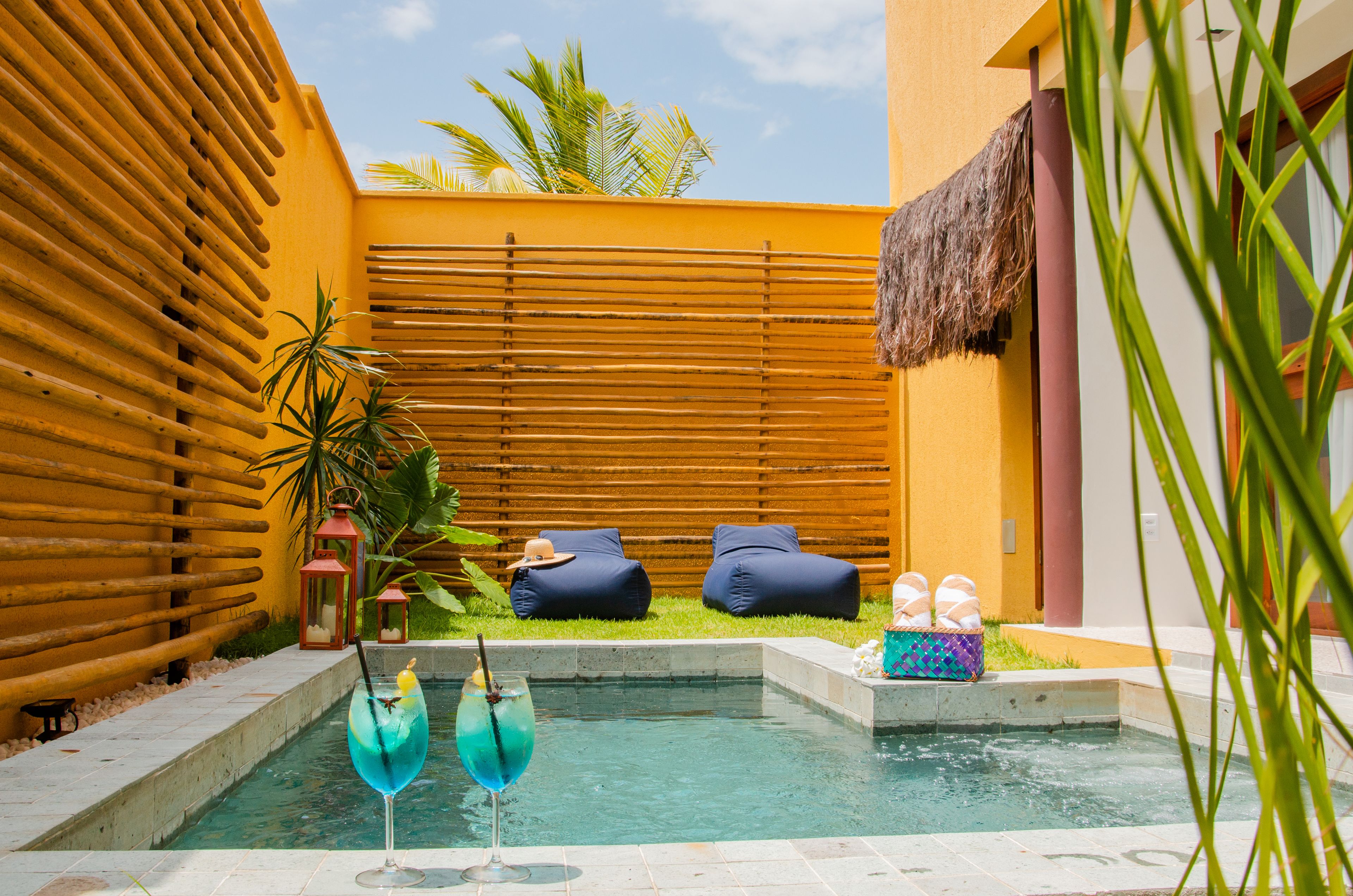 A pool area with a thatched roof, wooden slats, and lounge chairs.