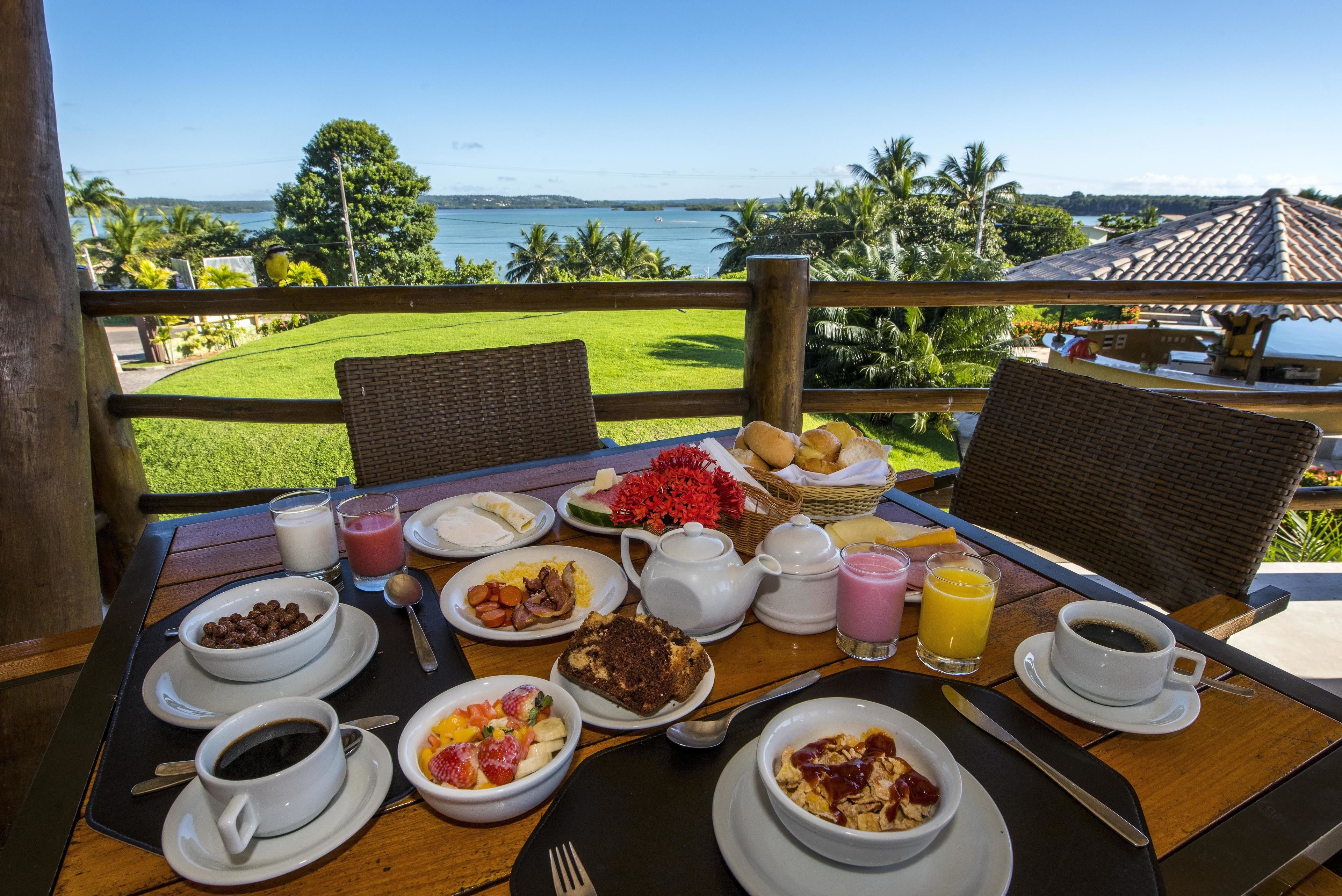 A breakfast table with various dishes, a view of the ocean, and a tropical landscape.