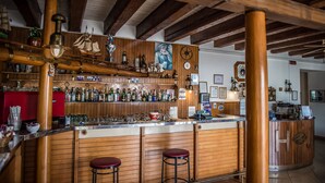 Un bar avec des poutres en bois, un comptoir en bois et des tabourets. On peut voir des bouteilles et des verres sur les étagères.