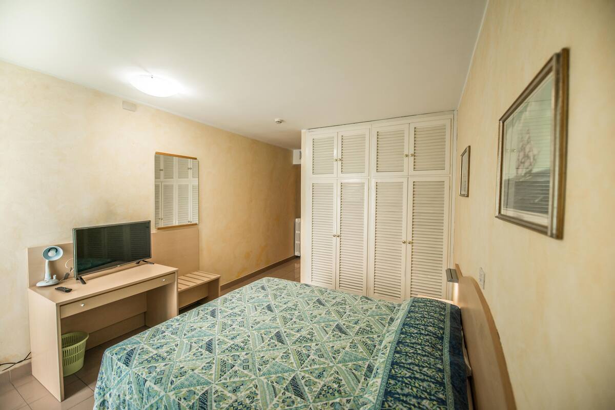 Une chambre à coucher comprenant un lit, un bureau, une télévision et une armoire.