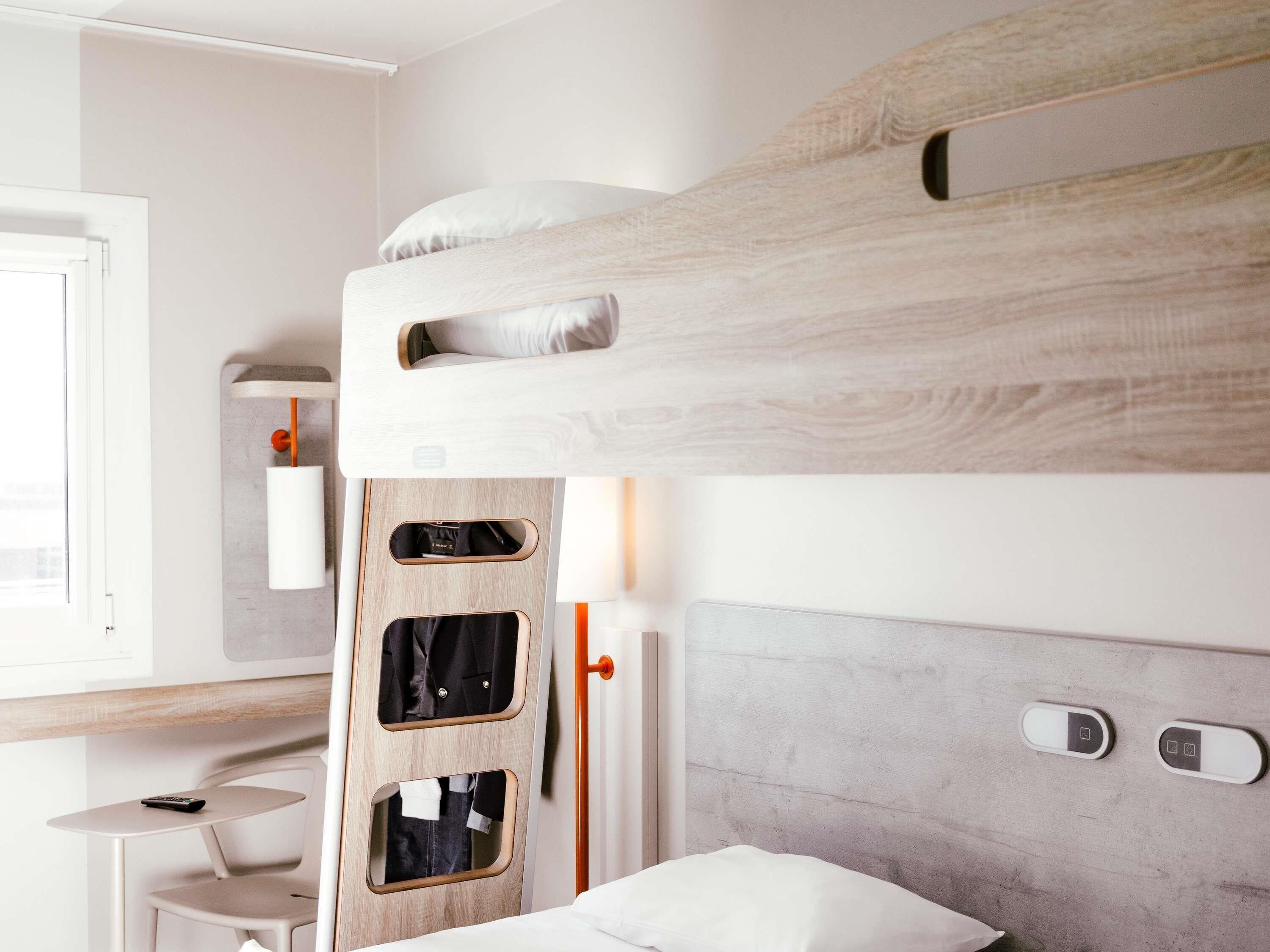A bunk bed with a wooden headboard, a bedside table with a lamp, and a small chair.
