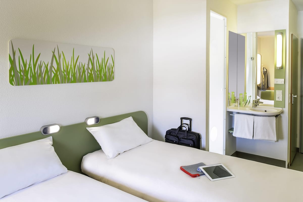 A hotel room with a bed, a bedside table with a lamp, a suitcase, and a bathroom with a mirror and sink.