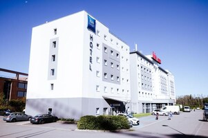 A modern hotel with a white facade, multiple floors, and a prominent "Ibis Budget" sign.