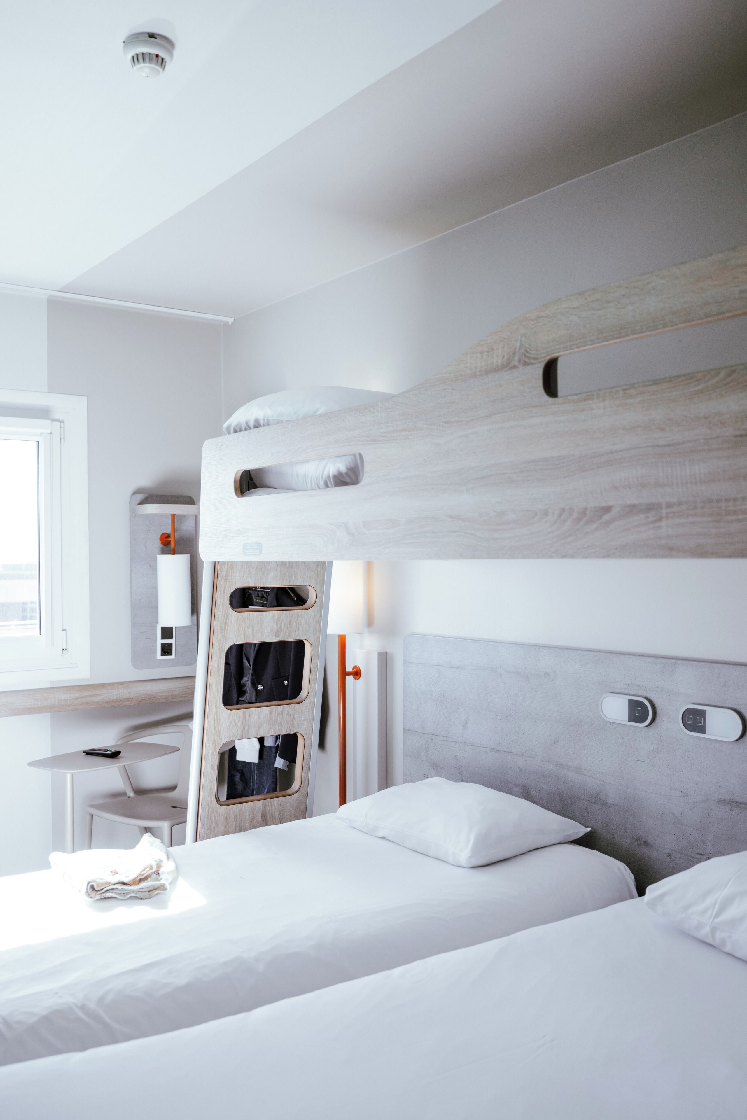 Una habitación de hotel moderna con literas, un escritorio y una silla, y una ventana.