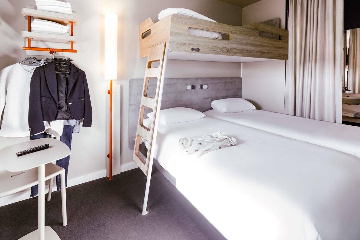 Una habitación de hotel con literas, un escritorio con silla, un perchero y una mesita de noche.