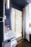 A hotel bathroom with a white sink, a glass shower enclosure, and a dark blue wall.