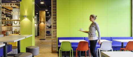 Una cafetería moderna con suelo de madera, paredes verdes y diversas opciones de asientos, incluyendo mesas y sillas.