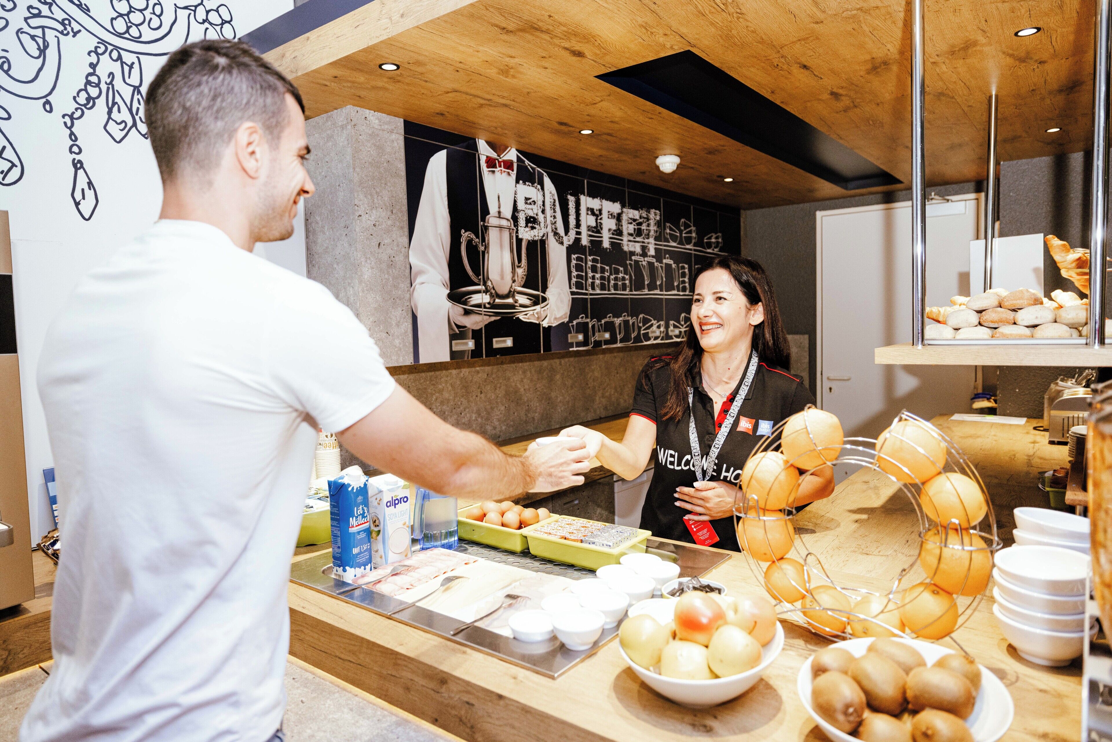 Mostrador de buffet con diversos alimentos y un empleado atendiendo a un cliente.