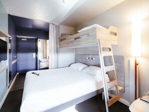 Ein Etagenbett mit Holz-Kopfteil, ein Nachttisch, eine Lampe und ein Badezimmer mit Waschbecken und Spiegel.