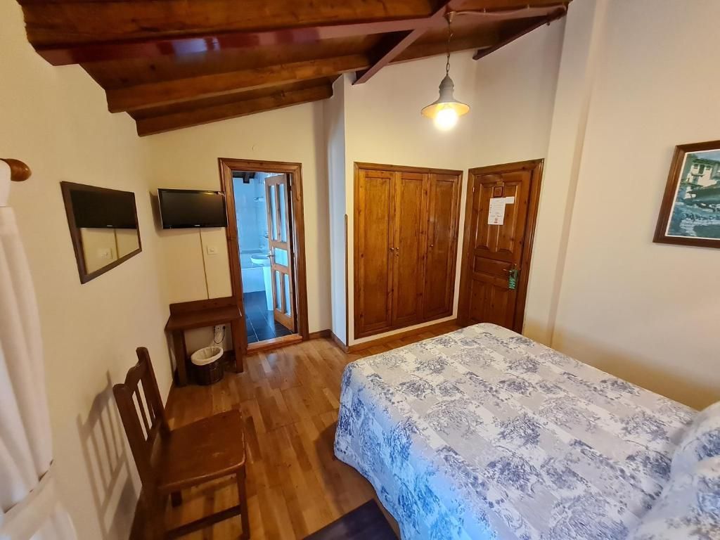 Un dormitorio con cama, armario de madera, televisor y una puerta que da a otra habitación.