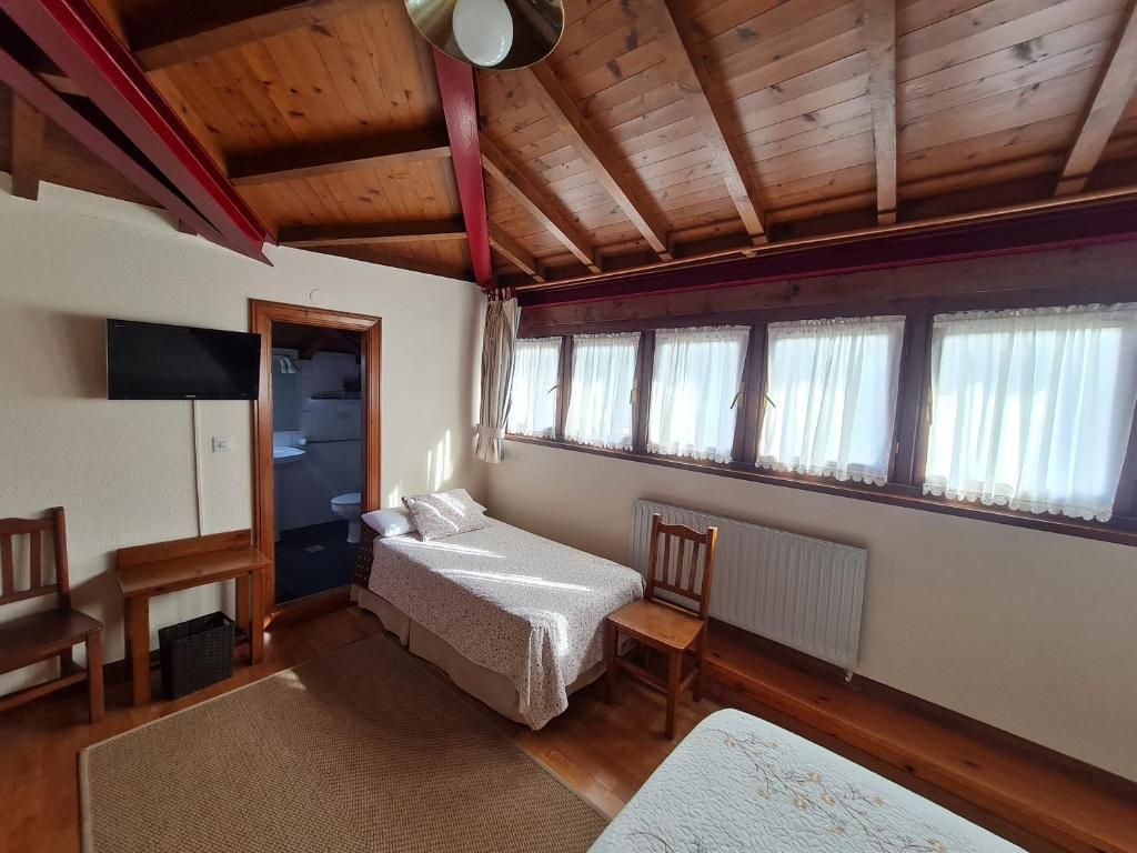 Une pièce avec un plafond en bois, un lit, une chaise, une petite table et une fenêtre avec des rideaux.