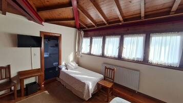 Habitación con techo de madera, una cama, una silla, una mesita y un ventanal con cortinas.