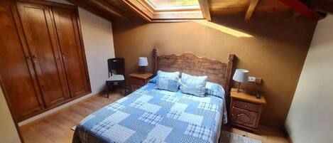 A bedroom with a skylight, wooden wardrobe, bedside tables, and a bed with a checkered bedspread.