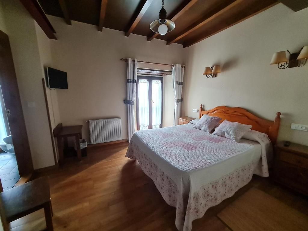 A bedroom with a wooden floor, a bed with a floral bedspread, a window with curtains, and a ceiling fan.