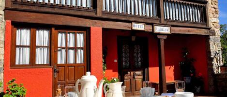 Un hotel con fachada roja, un balcón con barandillas de madera y una mesa puesta para el desayuno en el exterior.