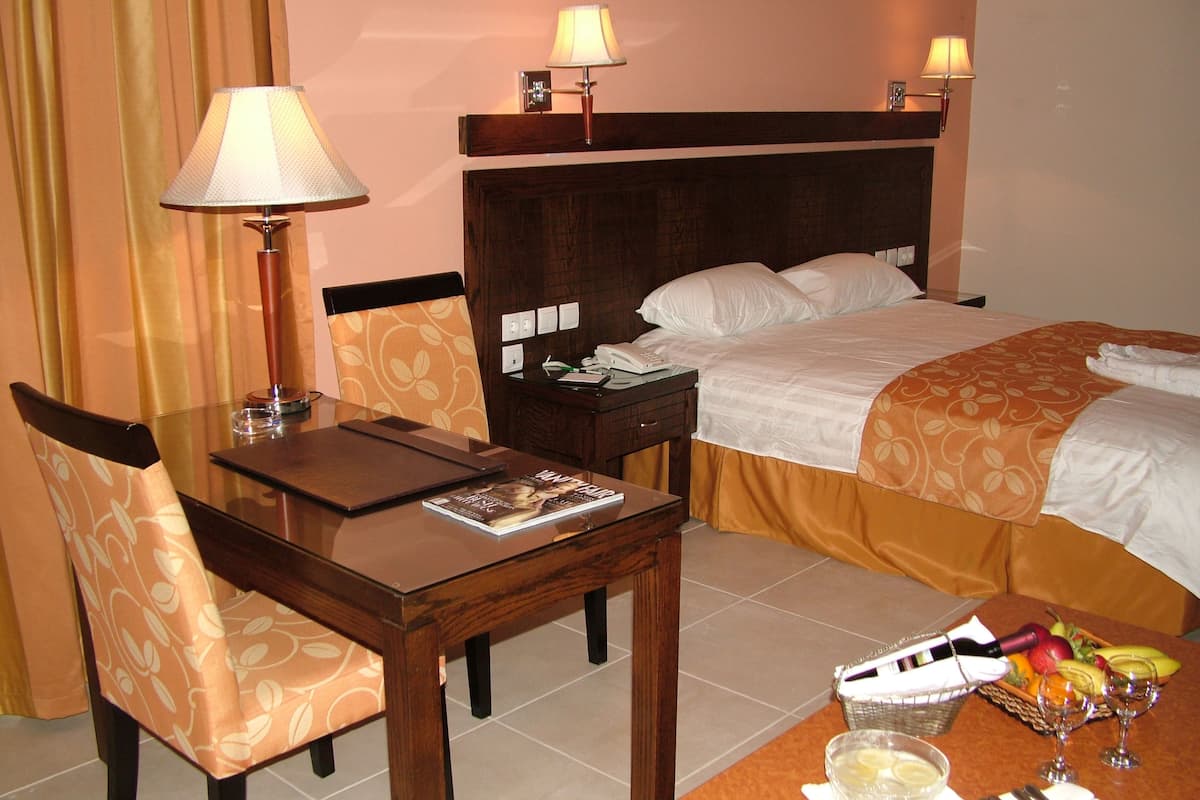 Habitación de hotel con cama, escritorio con lámpara, silla, mesita de noche con frutero y minibar.