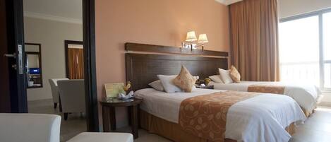 A hotel room with two beds, a sitting area, and a view of the outside.