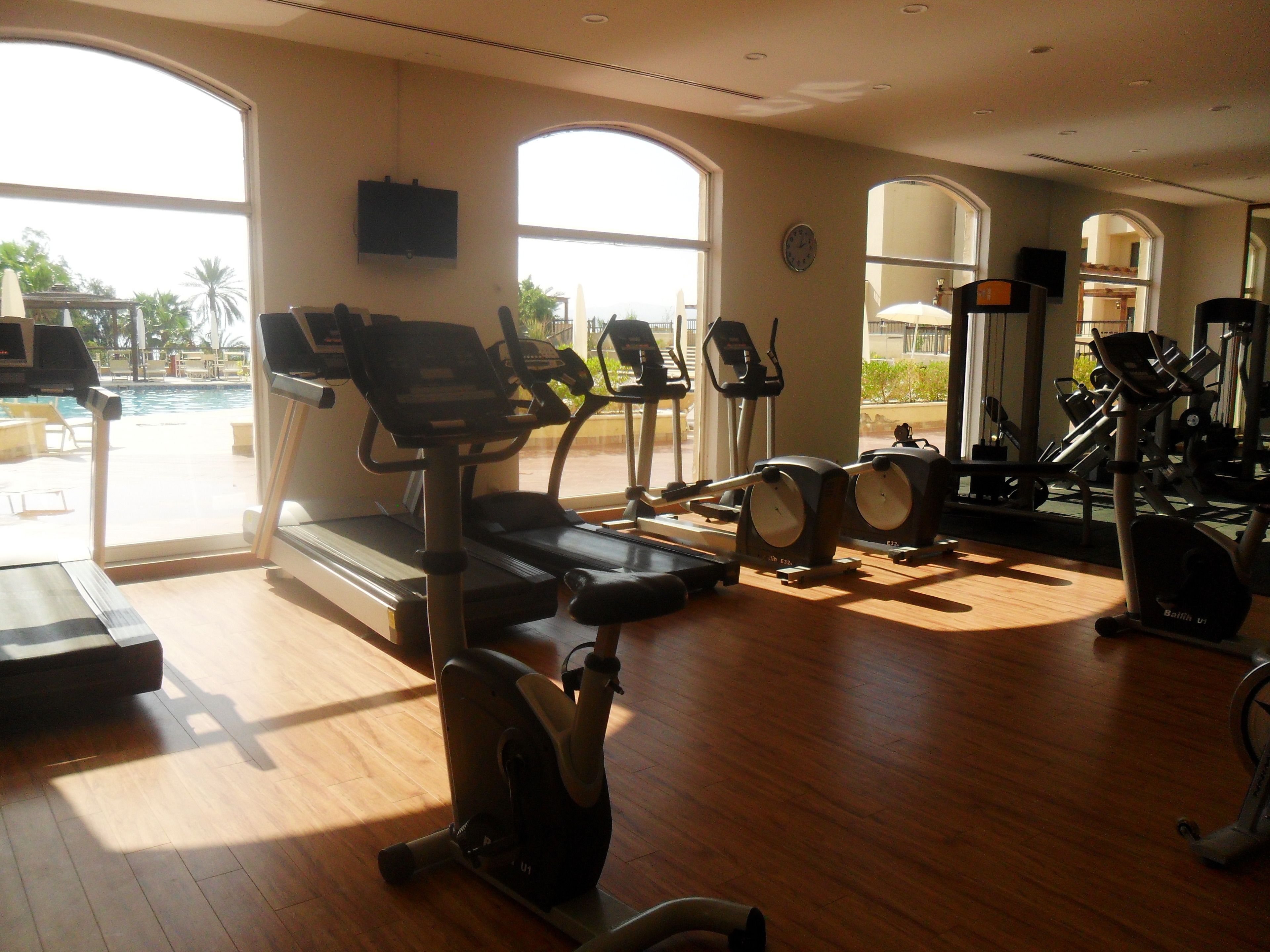 Gimnàs amb màquines cardiovasculars, vista a la piscina i un gran mirall.
