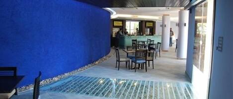 Un hall de hotel con una pared azul, una mesa de recepción y una zona de estar con sillas y una mesa.