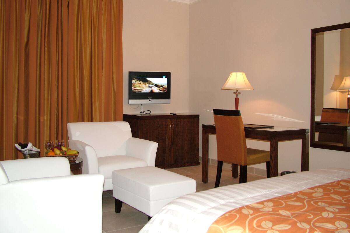 Una habitación de hotel con cama, escritorio, silla, televisor y lámpara.