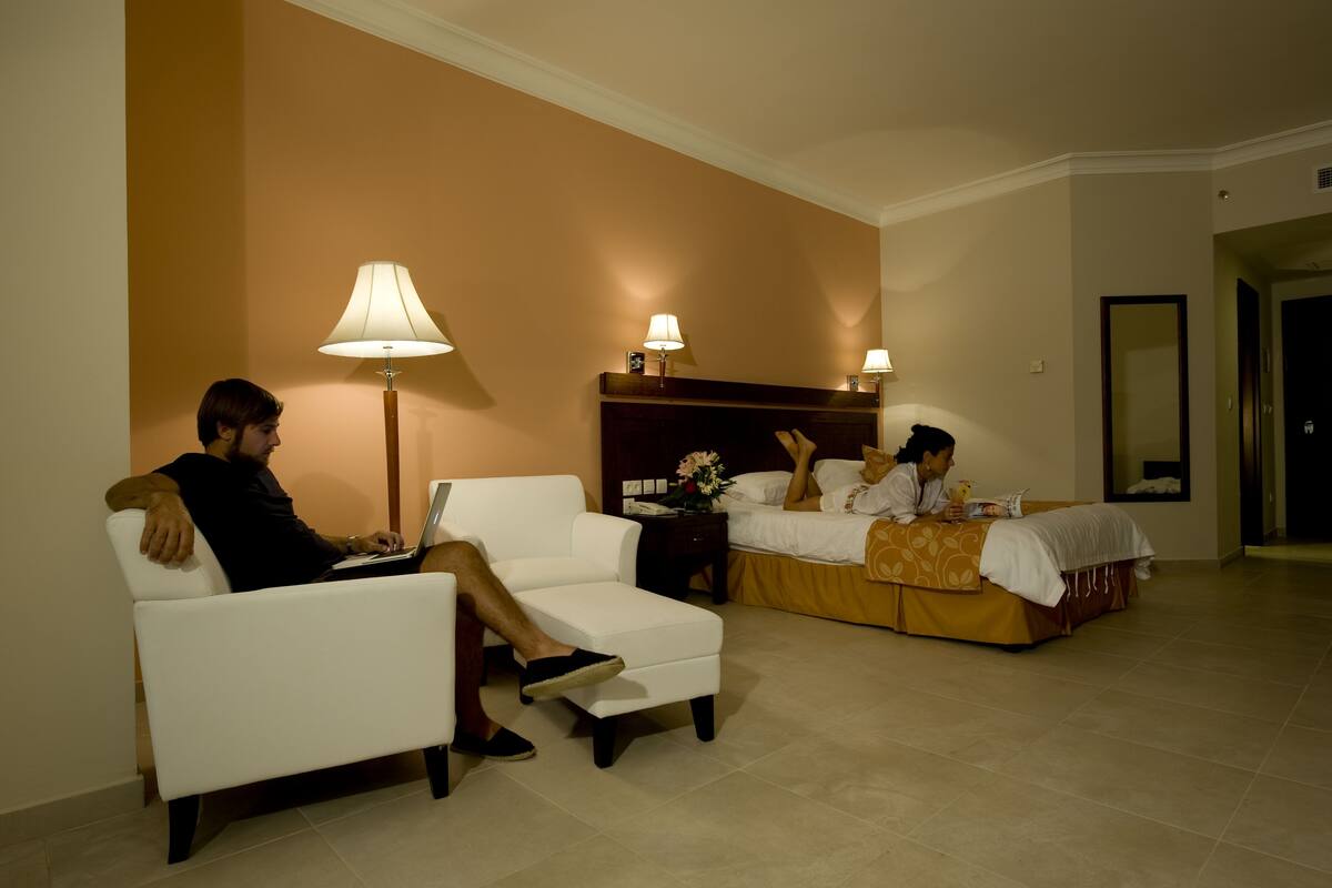 Una habitación de hotel con un sofá blanco, una cama con colcha amarilla y dos lámparas de noche.