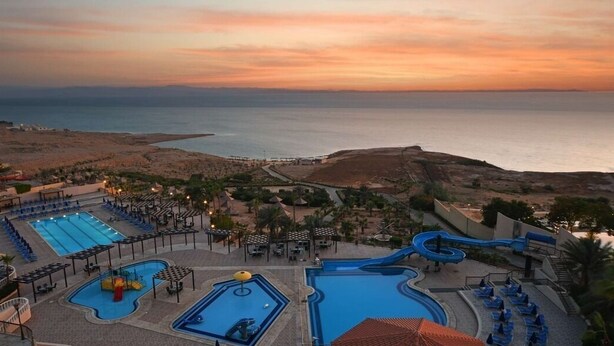 A resort with multiple swimming pools, a water slide, and a view of the sea at sunset. - Dead Sea Spa Hotel (Sweimeh)
