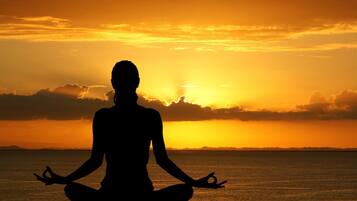 Silueta de una persona meditando en la playa al atardecer.