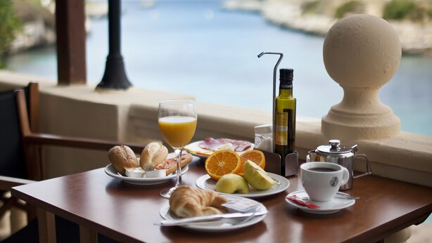 A table set with breakfast items, a lamp, and a view of the sea. - Cala Bona & Mar Blava Hotels (Ciutadella de Menorca)