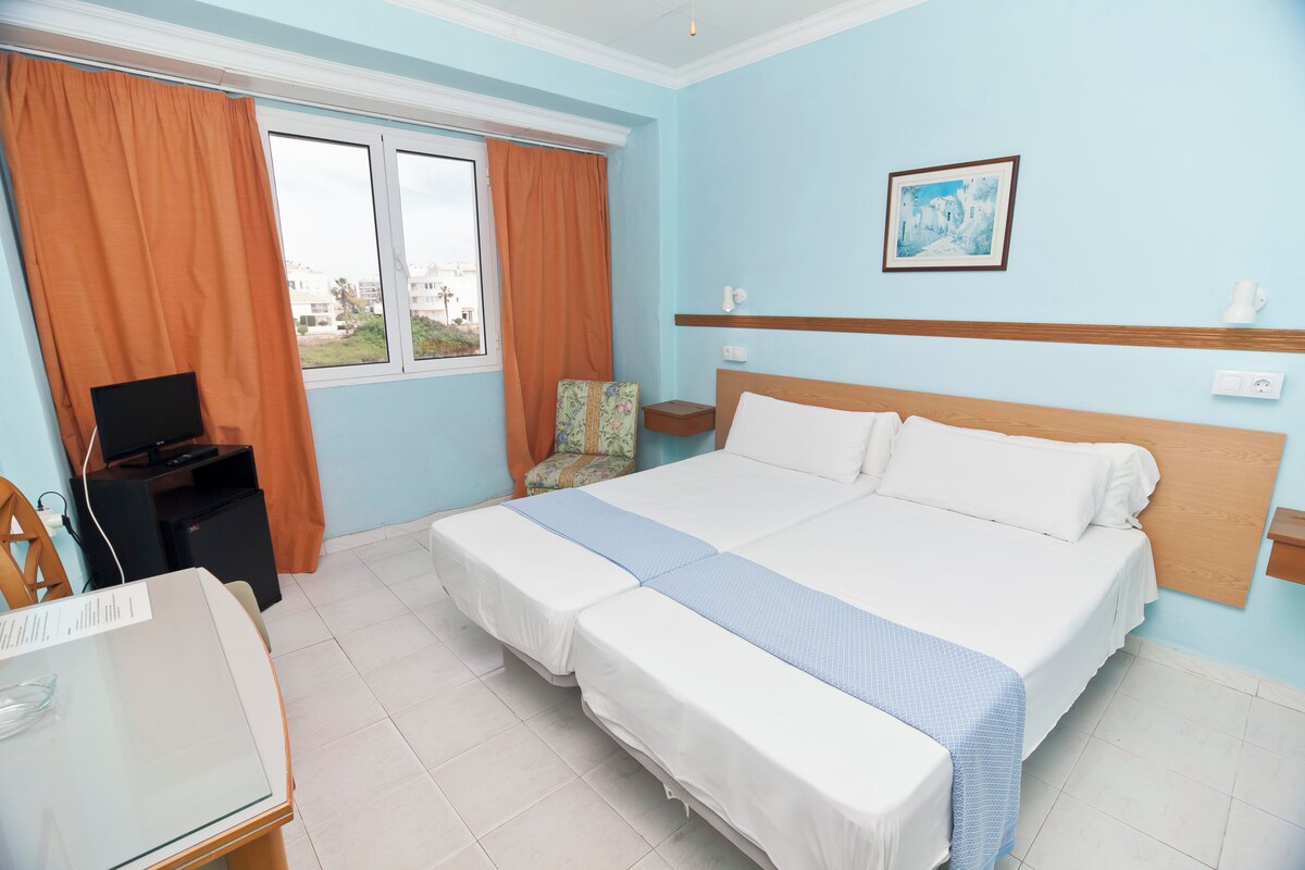 Habitación de hotel con una cama grande, un escritorio con computadora, una silla y una ventana con cortinas.