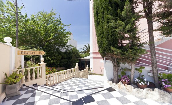 A reception area with a checkered floor, a sign reading "RECEPCIÓN", and a white building with a pink facade. - Cala Bona & Mar Blava Hotels (Ciutadella de Menorca)