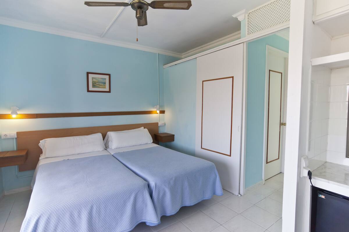 Ein Schlafzimmer mit Bett, Nachttischen, Deckenventilator, Gemälde und einer Tür.