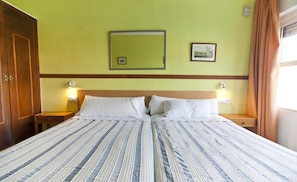 Un lit double avec une couvre-lit à rayures, deux tables de chevet avec des lampes, une tête de lit en bois et un tableau encadré au mur.