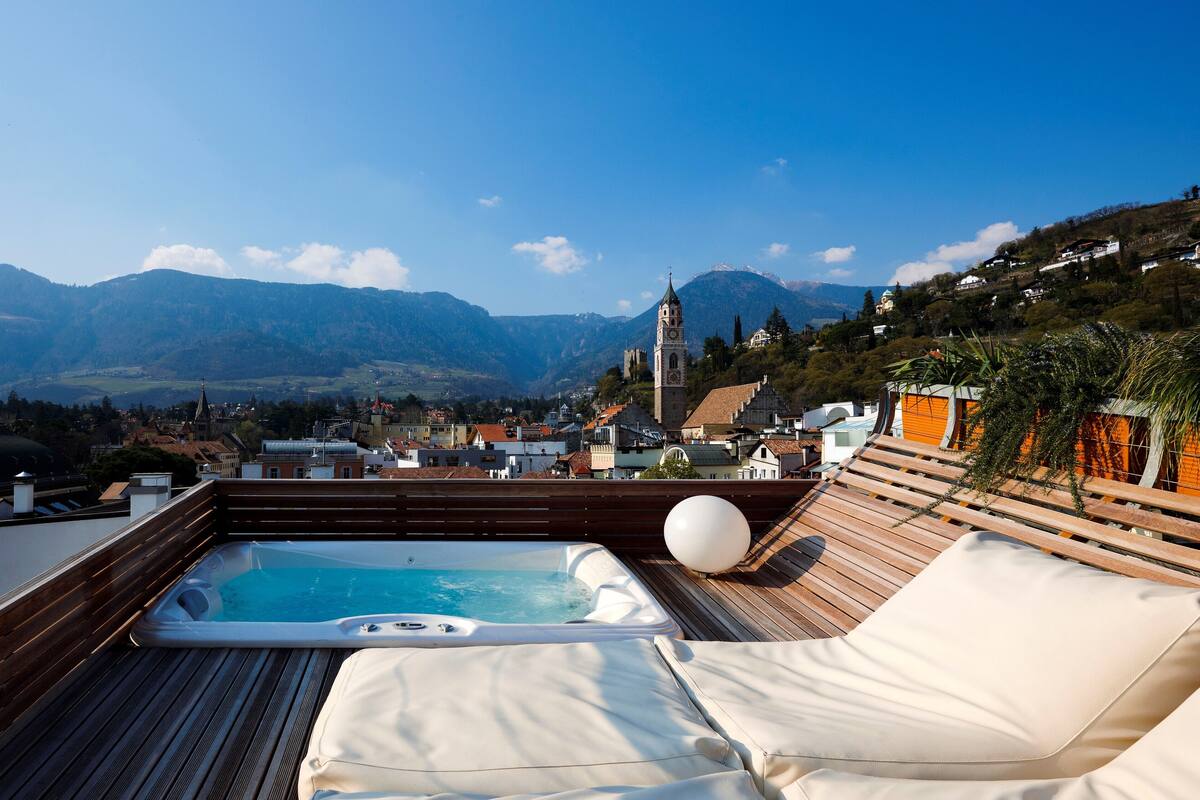 Una terraza en la azotea con un jacuzzi, sillas de descanso y una vista panorámica a las montañas.