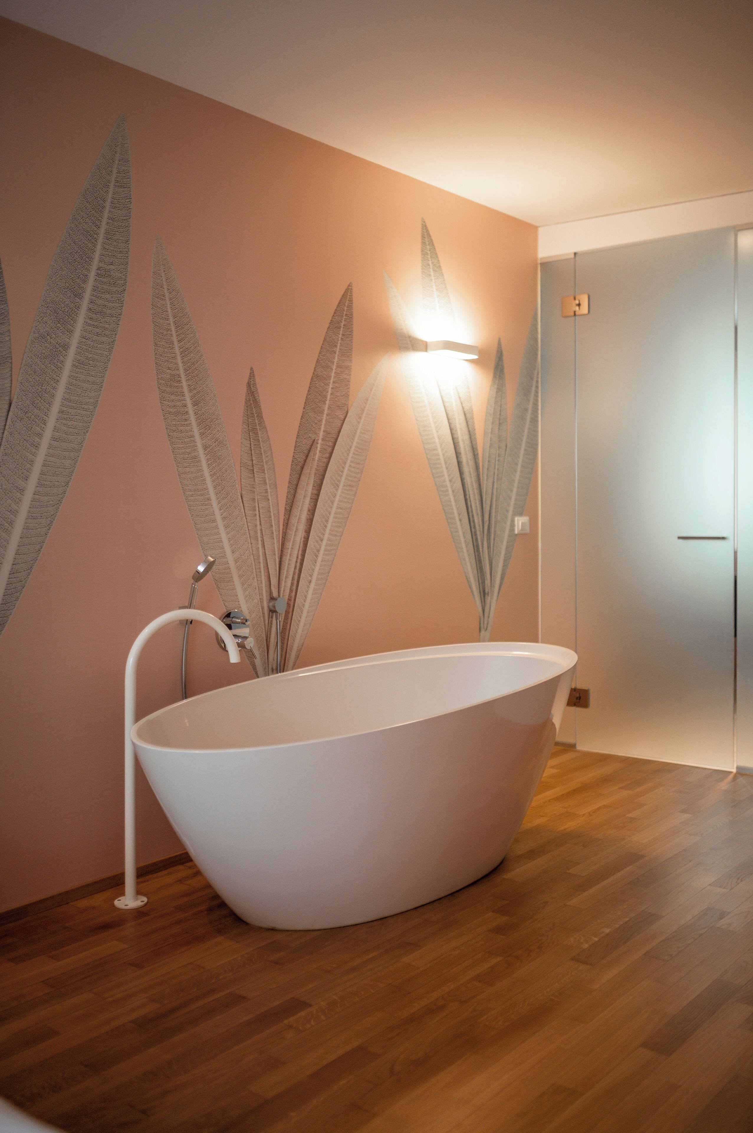 Un baño moderno con una bañera independiente, piso de madera y un aplique de pared.