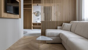 A modern living room with a sofa, a TV mounted on the wall, and a wooden partition with a mirror. - ImperialArt (Merano)