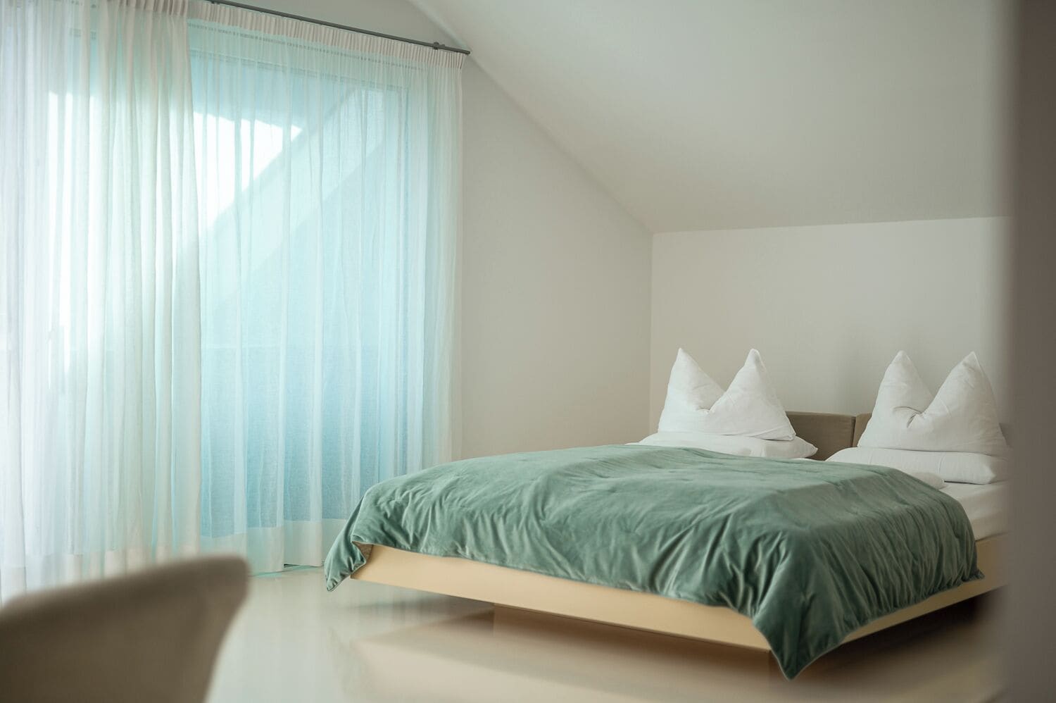 Un dormitorio moderno con cama, almohadas blancas y cortinas de gasa.