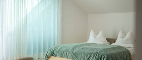 Un dormitorio moderno con cama, almohadas blancas y cortinas de gasa.