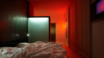 Quarto moderno com cama bem arrumada, porta que dá para outro espaço e luminária fixada na parede.