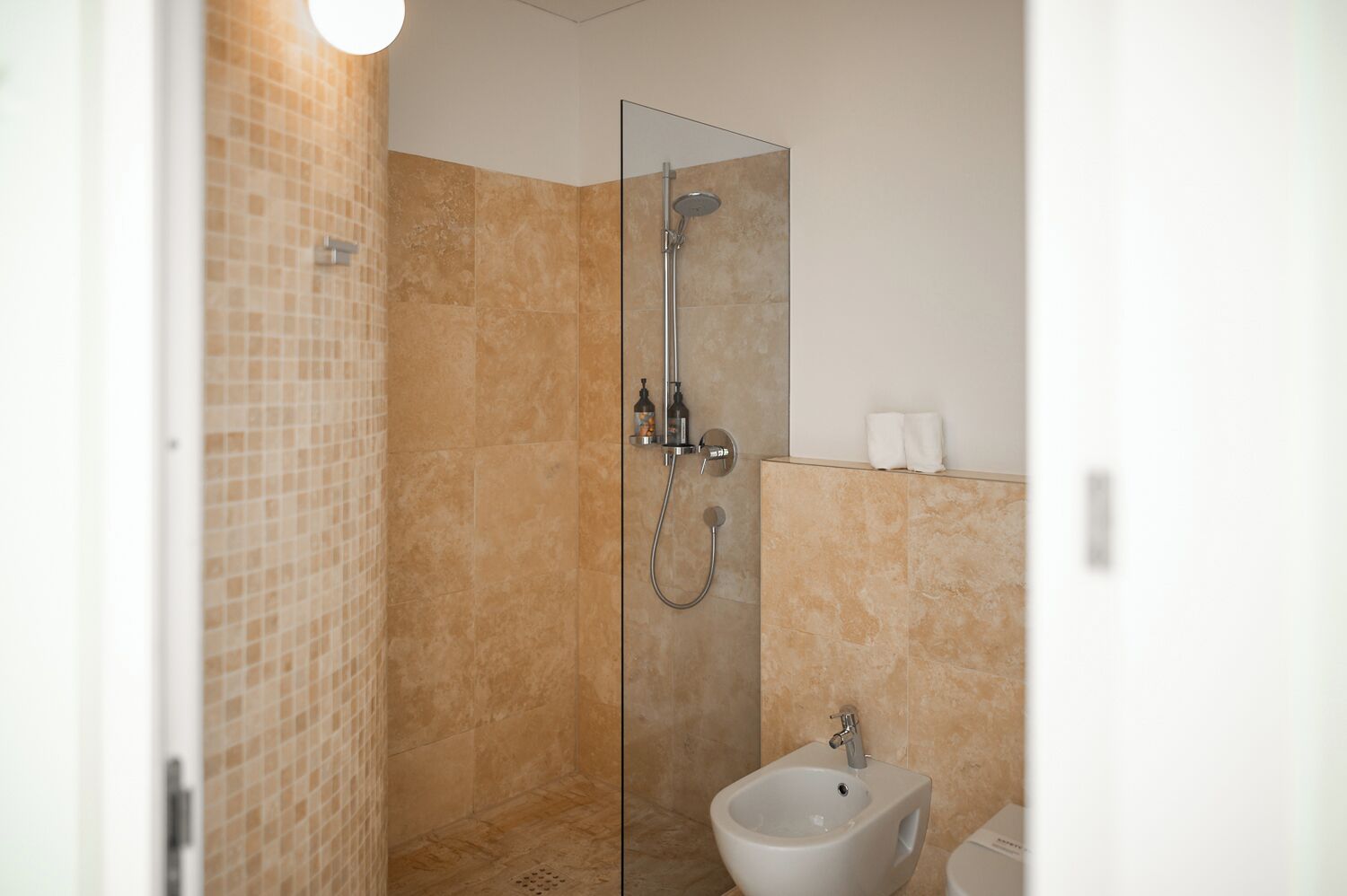 Un baño moderno con cabina de ducha de vidrio, un bidé y suelo de baldosas.