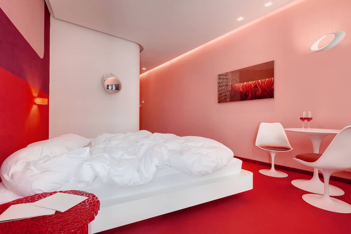 Una habitación de hotel moderna con una cama grande, una pequeña mesa con sillas y una obra de arte colgada en la pared.