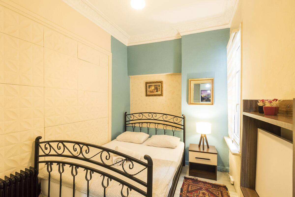 Une chambre à coucher comprenant un lit, une table de chevet, une lampe, un tableau encadré au mur et une fenêtre donnant sur un paysage.