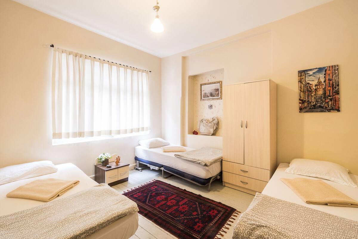 Une chambre avec deux lits, une armoire en bois, une table de chevet et une fenêtre avec des rideaux.