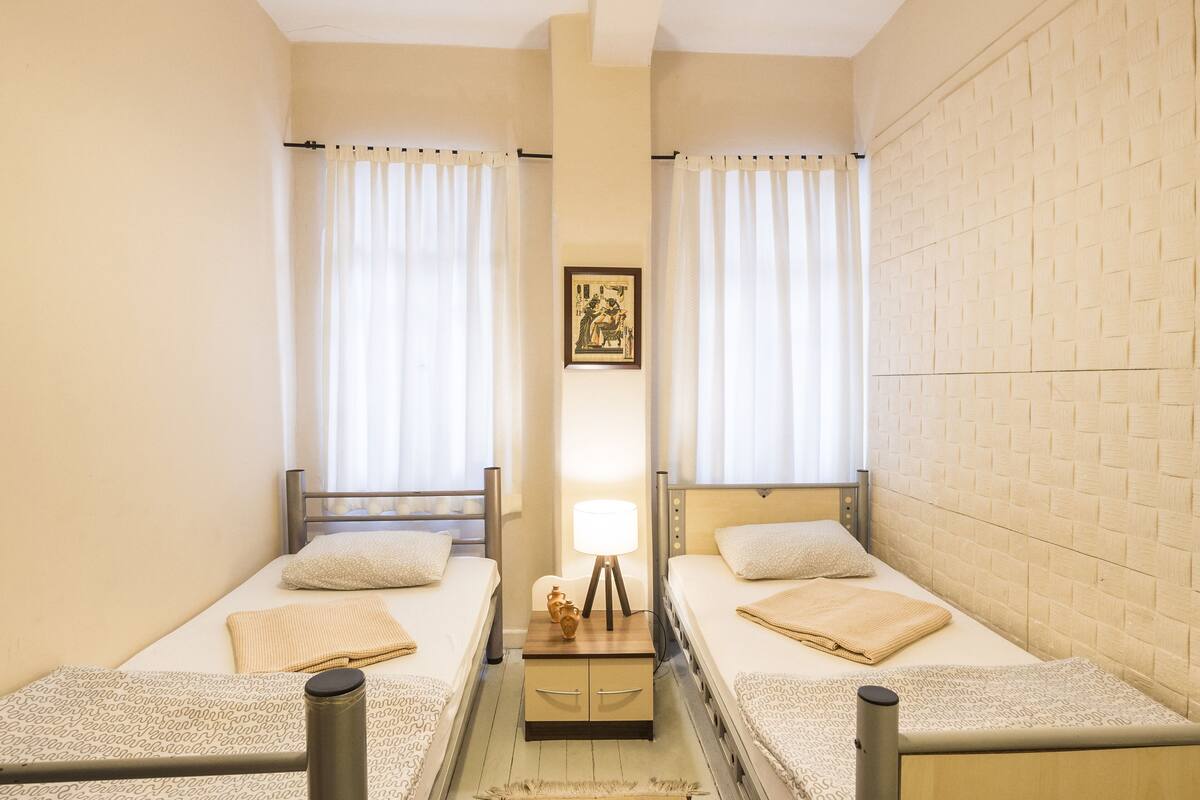 Une chambre double avec deux lits simples, une table de chevet avec une lampe et un tableau encadré au mur.
