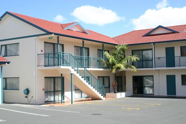 A two-story motel with a red-tiled roof, a palm tree, and a parking lot.