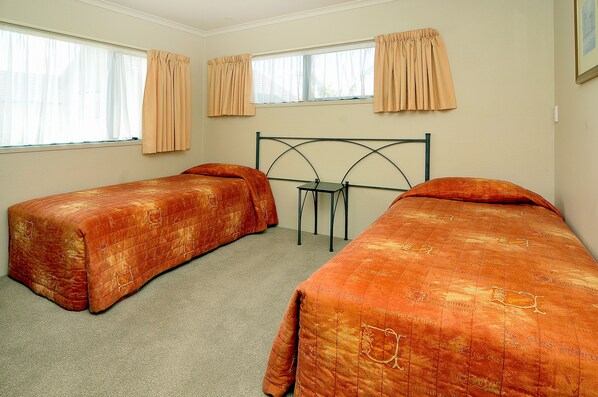 Un dormitorio con dos camas individuales, una mesita de noche y una ventana con cortinas.